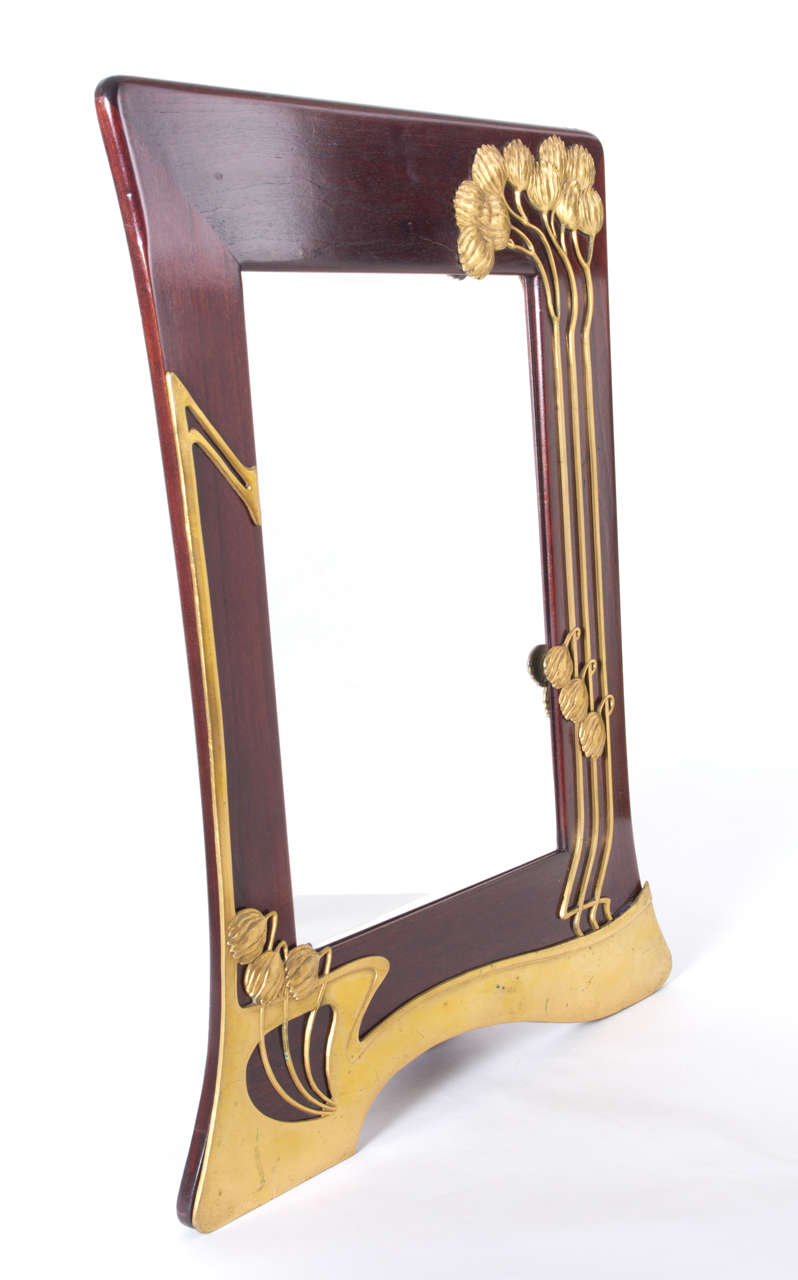 Mahogany framed mirror with gilt pewter Art Nouveau stylized flower and whiplash motif.