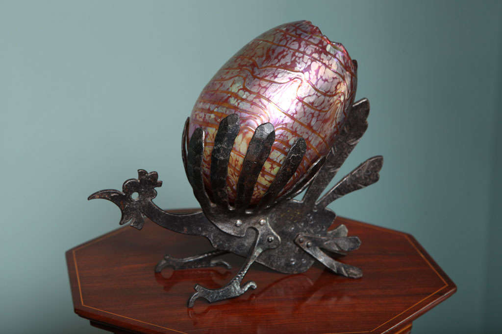 A whimsical Austrian Art Nouveau glass and wrought iron vase by, Loetz the base in the form of a stylized rooster with a highly decorated red oil spot and threaded glass shaped egg by Loetz on its back. The vase is unsigned.