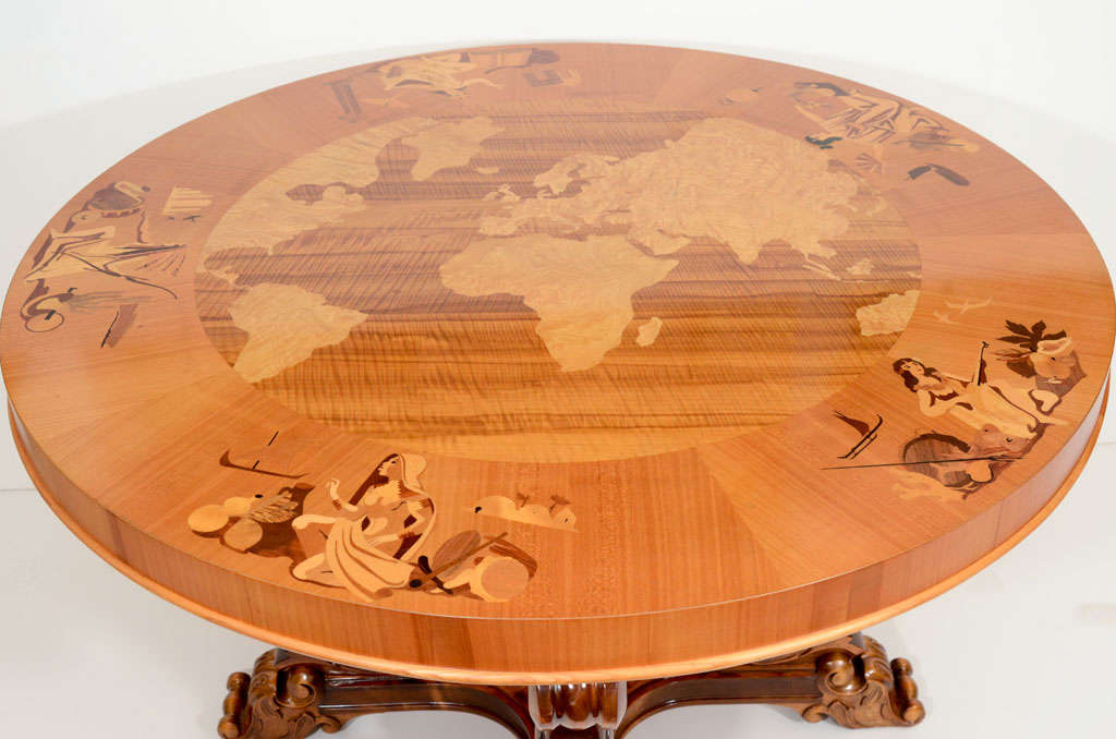 Circular, with an inlaid globe of various exotic woods and a deep border inlaid with female figures representing the Americas, Asia, Oceania, Europe and Africa. The birch banded top rests on a four-part base of fabulous ocean creatures and wavelike