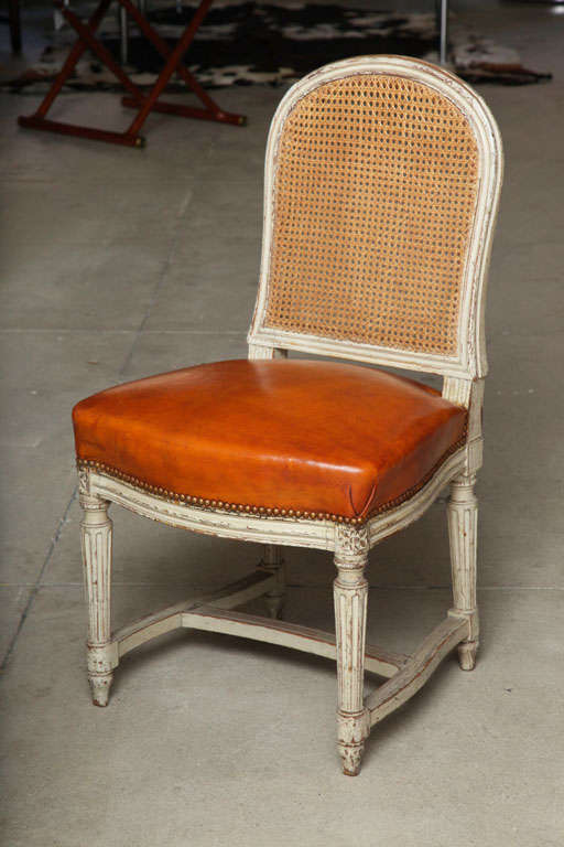 A pair of Louis XVI Style painted side chairs with caned back and leather seat in a beautiful cognac color.