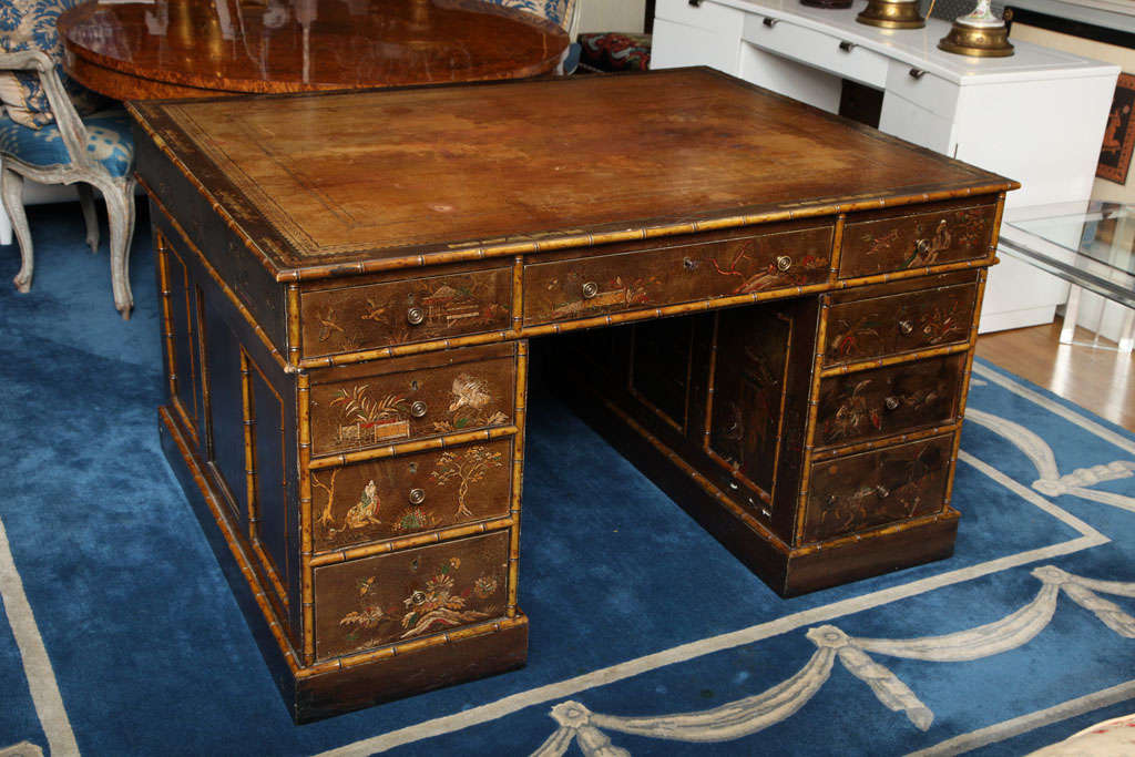 An English Regency period double pedestal partners desk with faux bamboo molded edges and raised Chinoiserie decoration on a brown ground. The top with inset tooled leather and the sides with recessed panels.