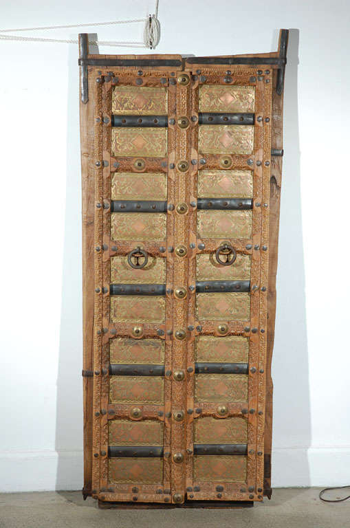 Pair of 19th Century Anglo Indian Doors or window.
Moorish Rajasthan work carved teak bound with hand-wrought iron, brass studs and iron bands, carved brass decorated panels.
Nice patina.
Could be hang on a wall as a decorative piece.