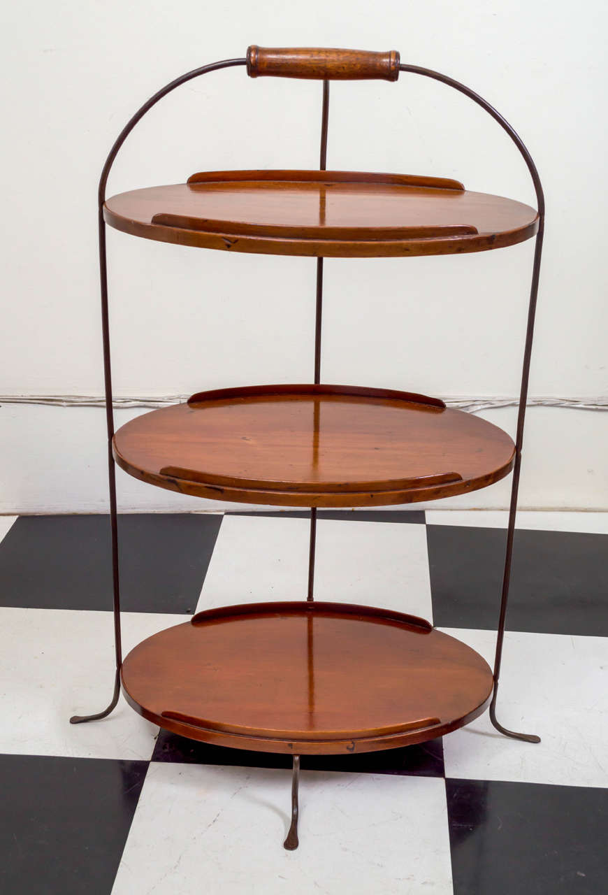19th century English petite three-tier server. The three mahogany trays each fitted with small front and rear galleries. All of the trays are joined by brass legs that terminate with a wood handle on top and the bottoms splay out in wrought splayed