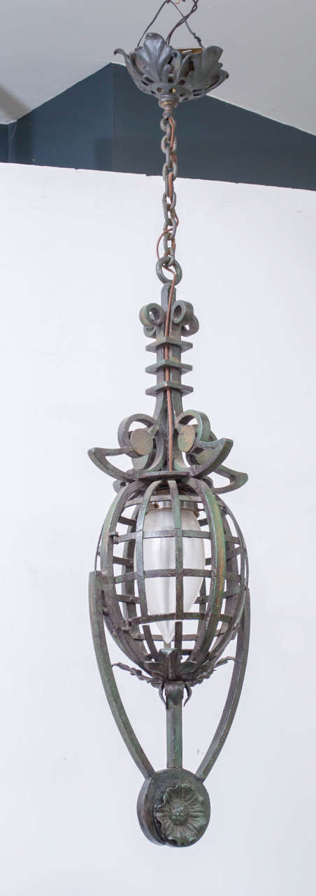 Early 20th century Continental (French or German), iron and paint drop pendant chandelier. Heavy wrought iron and riveted construction, retaining the old dark green paint. All rewired with a period Holophane torpedo form globe that intensifies the