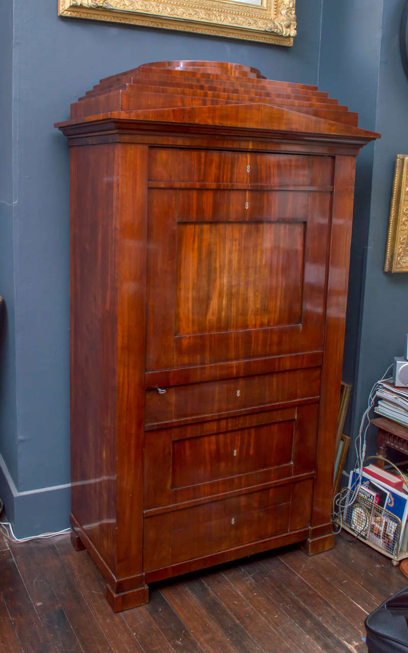 19th century German Biedermeier mahogany cabinet. Classic lines with good small proportions. French polished finish. 
The door in the design detail facade of a secretary abattant with drawers below. Opens to an interior fitted with four adjusting or