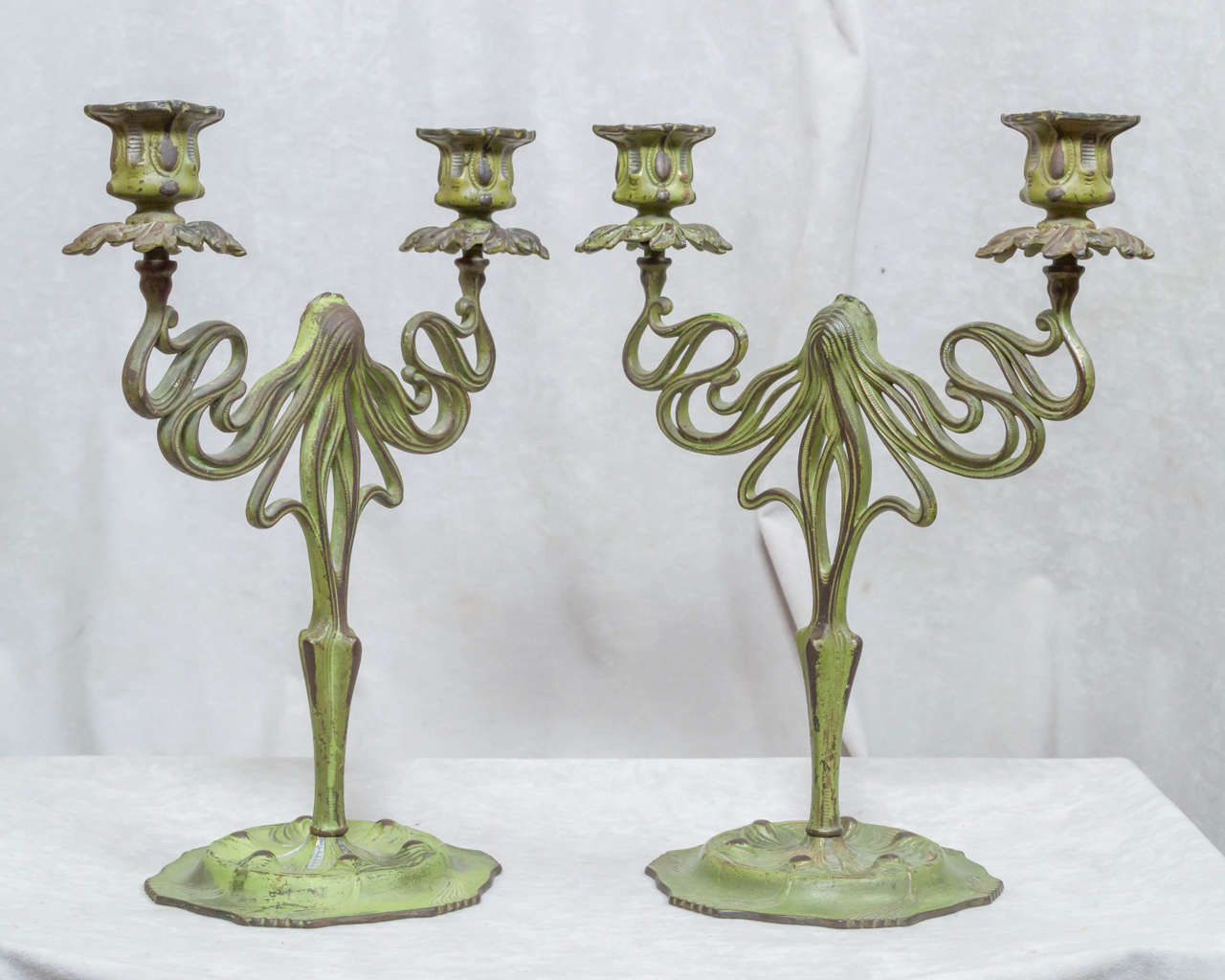 This lovely, sinewy pair of candlesticks demonstrates the allure of Art Nouveau. Having curvilinear lines and the sweet cameo of the woman's face in the center are so very appealing. They have their original green factory applied patina. Similar