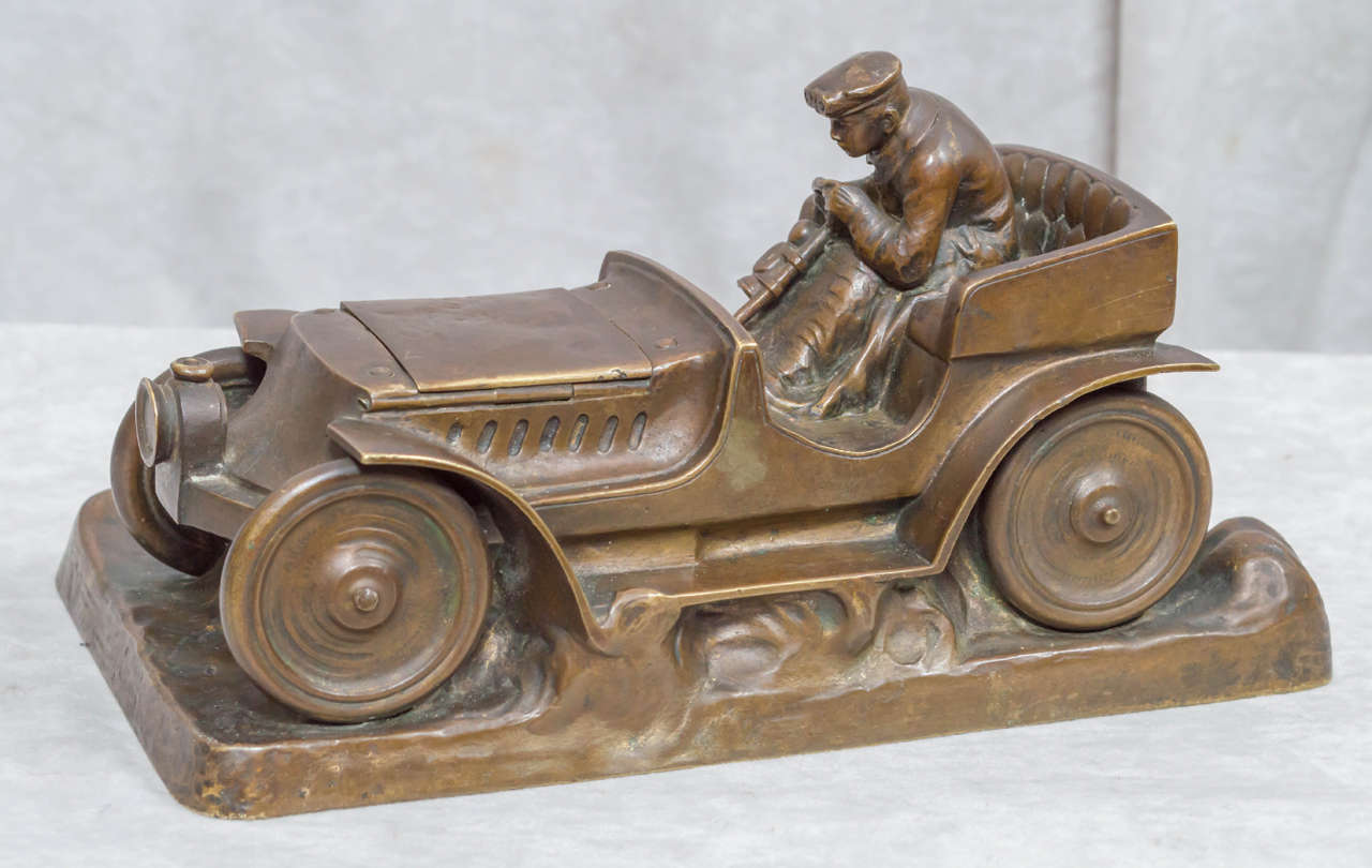 Oh how rare this subject matter in sculpture appears. We would like to point out that this no small trinket. It is impressive and good sized. The driver is a kick and the car is certainly from the period. The hood opens up to reveal an inkwell. A