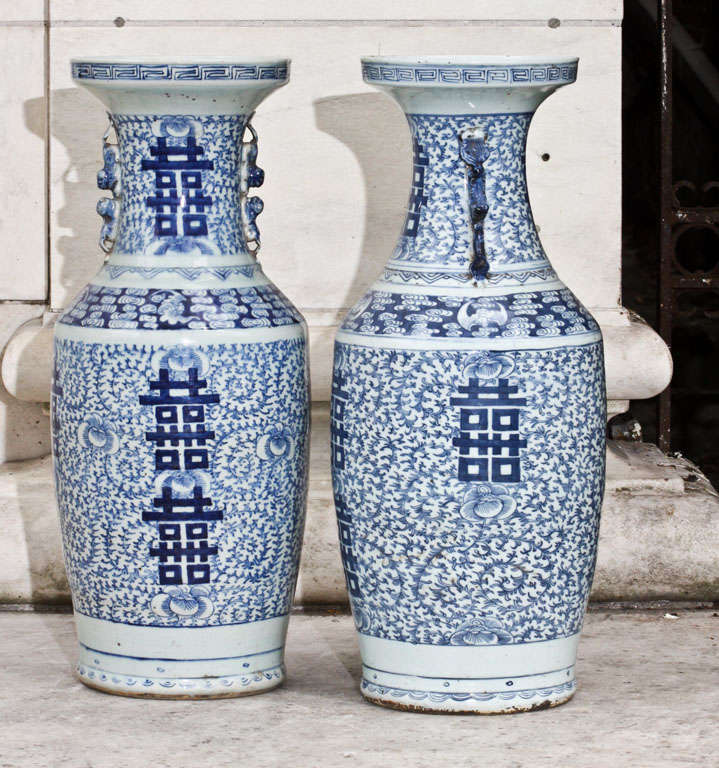 This beautiful pair of large vases displaying the double happiness symbol are finely painted in the blue and white colors so popular in the west. The body  and necks of each vase is done in an overall design of peonies within vining foliage and the