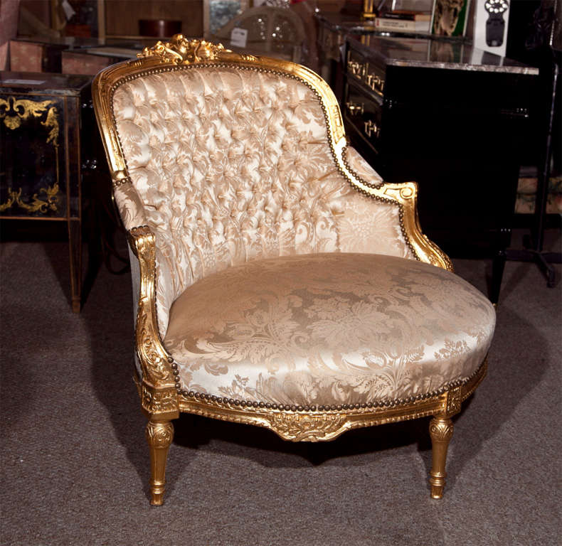 A French Louis XVI style giltwood corner chair, 20th century, upholstered in beige silk, downswept arms, tufted back and padded seat, raised on tapering bulbous legs.