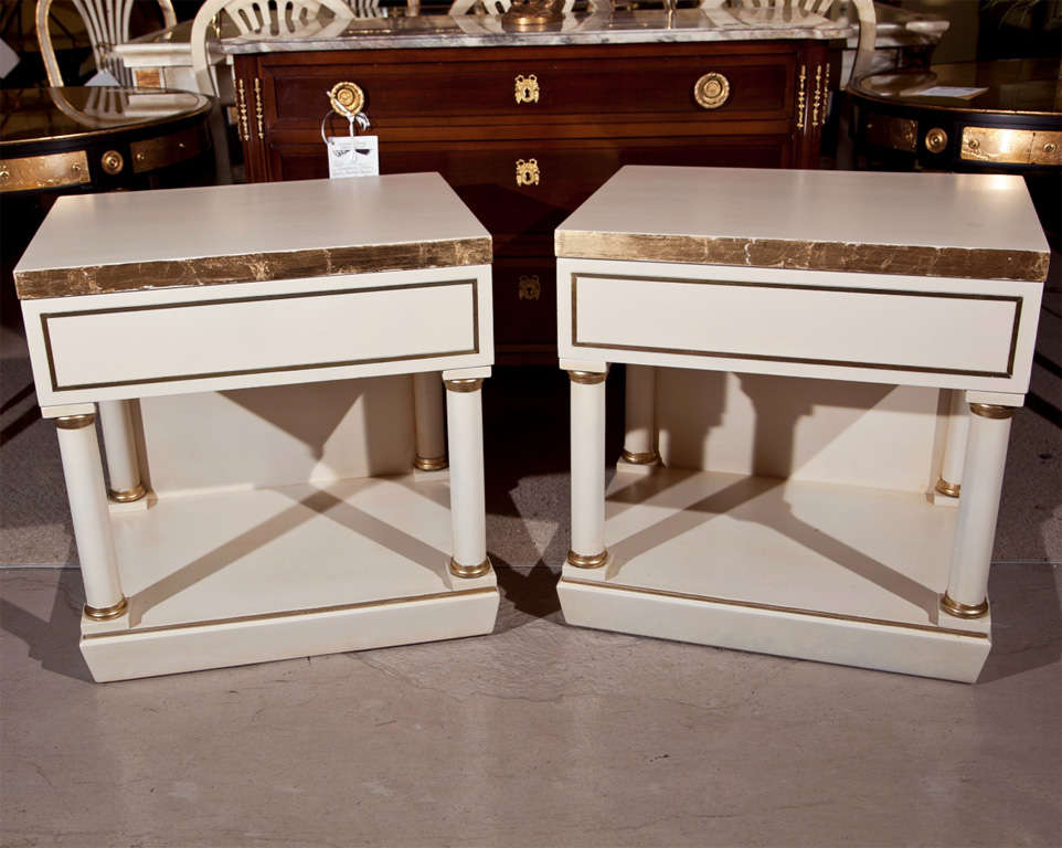 Pair of end tables/nightstands, overall white painted and parcel-gilt, attributed to Grosfeld Housee, the top over a single drawer supported by columnar uprights, raised on block base.