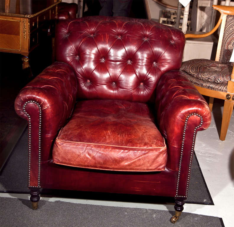 Pair of English red leather chesterfield club chairs, tufted back, rolled arms, cushioned seat, raised on wooden bulbous legs ending in brass castors.