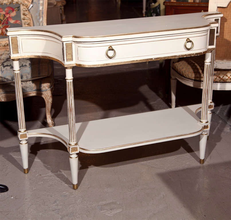 French Louis XVI style white painted and parcel-gilt serving console, the bow front with a single drawer flanked by concave sides, supported by four fluted columns joint with a lower tier, raised on tapering bulbous legs by Maison Jansen.