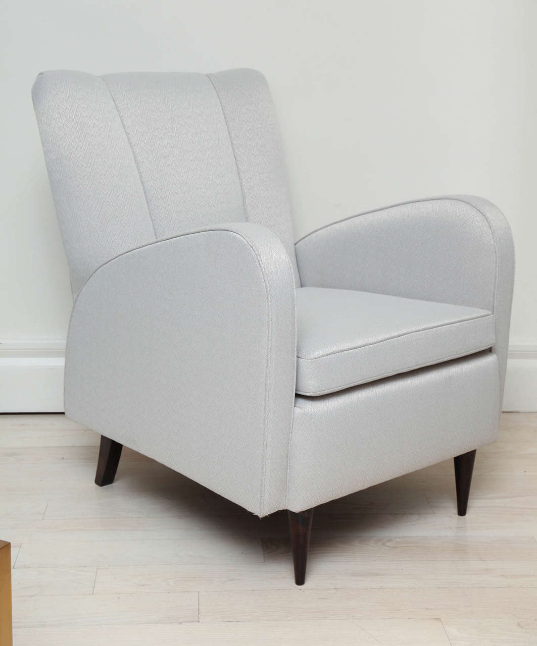 Pair of upholstered stylized Art Deco armchairs with shaped channeled backs and wood legs.