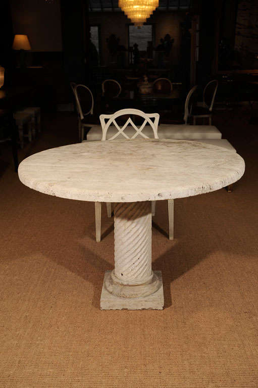 The circular top on a spiral form pedestal on a plinth base. The table of upolished travertine.  Note: Can be used outside.