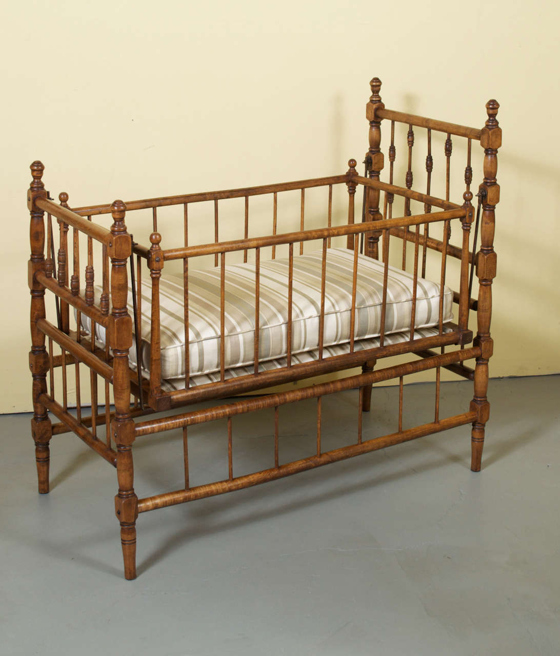A gorgeous country French swinging cradle with removable upholstered cushion. The swinging part of the cradle has nine wooden spindles on two sides and five wooden spindles on the other two sides. There are four steel rods, one in each corner, that