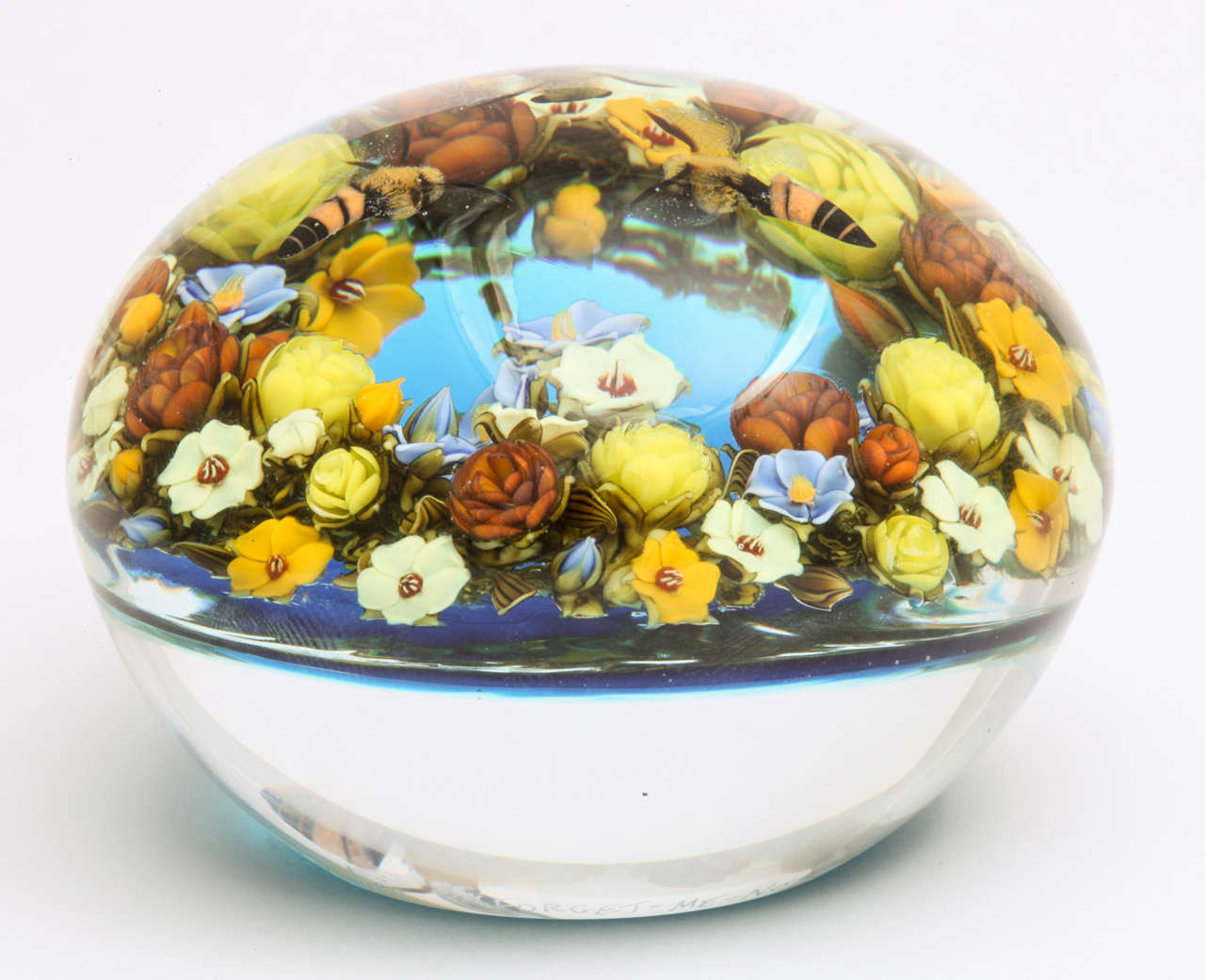 A beautiful David Graeber wreath bouquet paperweight with a bouquet of yellow and blue forget-me-nots and yellow roses around three central flowers and three hovering honeybees all on a translucent blue ground