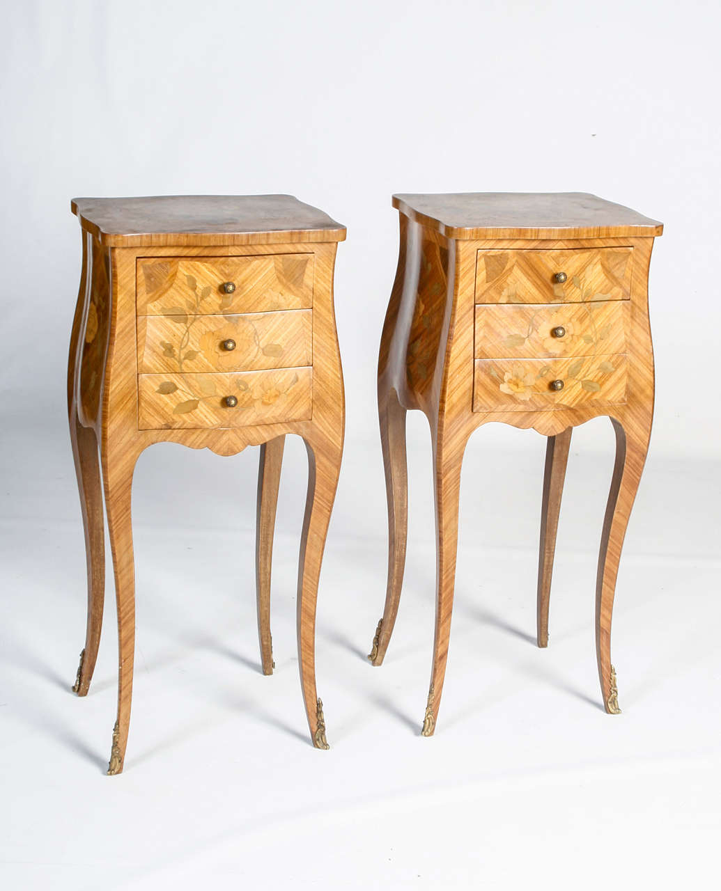 A superb pair of Louis XV Kingswood bedside tables with ormolu mounts. Intricite floral inlay and leaf patterns. Having three functional drawers. These are designed in a bombé shape.