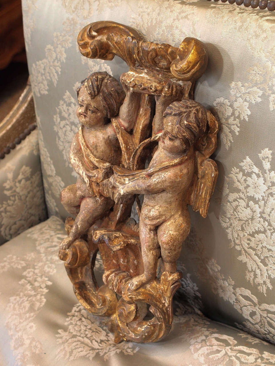 Fabulous polychrome carving of two putti standing on a gilt foliate garland, between a shell, holding a gilt crown.  Gilt is still visible but only a few spots
of paint remain.