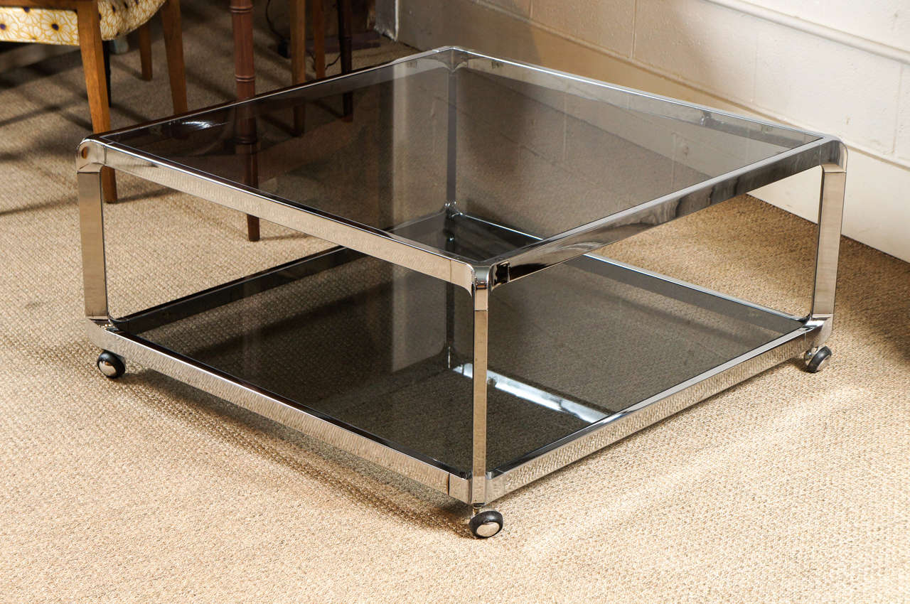 Here is a beautiful two tiered square chrome coffee table with a curved edge. The table features smoked glass and casters.