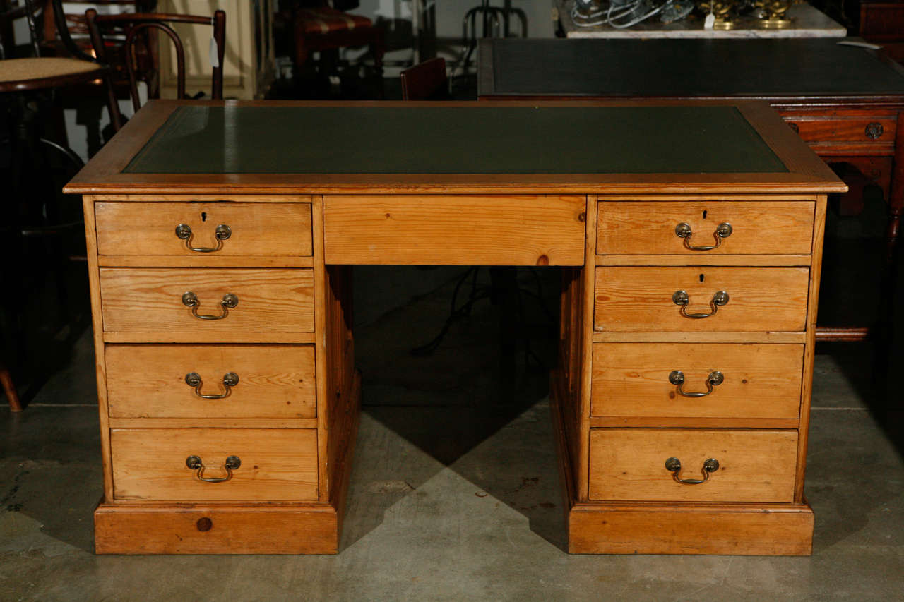 This large pine desk has a newly restored green leather top with two bands of gold tooling at the edge and is marked with a Great Western Railroad stamp. The desk has inset panels at the front and sides with plinth bases. The eight drawers have
