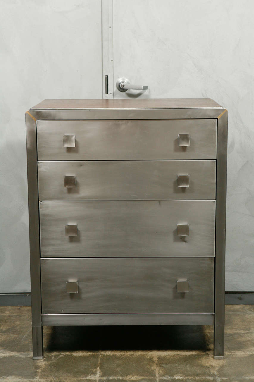 A good quality polished metal American chest circa the 1940's having; four drawers, a polished wood top, rounded shoulders, square metal knobs and raised on 5 1/2" square legs.