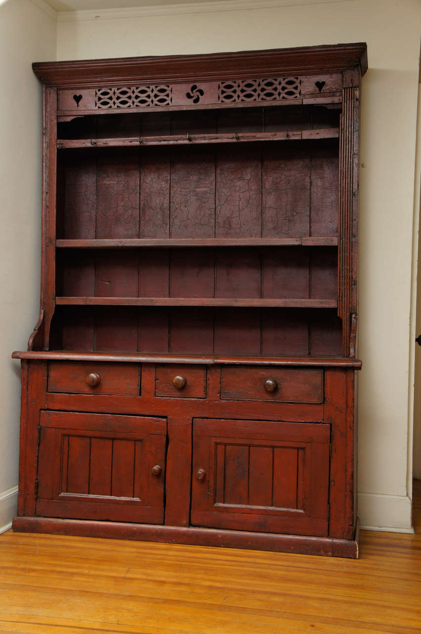 This may be the best step back cupboard we have ever had. Lovely in its original red paint, it dates 1780. The frieze at the top has lovely detail with two hearts, a swirl and lattice. It has three shelves, a nice counter space, below three drawers