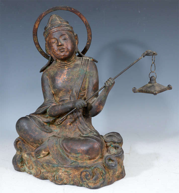 A sculpture of Buddha in gilt bronze. The piece sits with legs crossed and holds a censer.