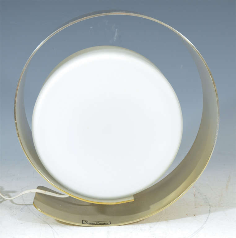 A circular design polished brass table lamp with white glass shade. The piece is by noted designer Pierre Cardin.
    
    