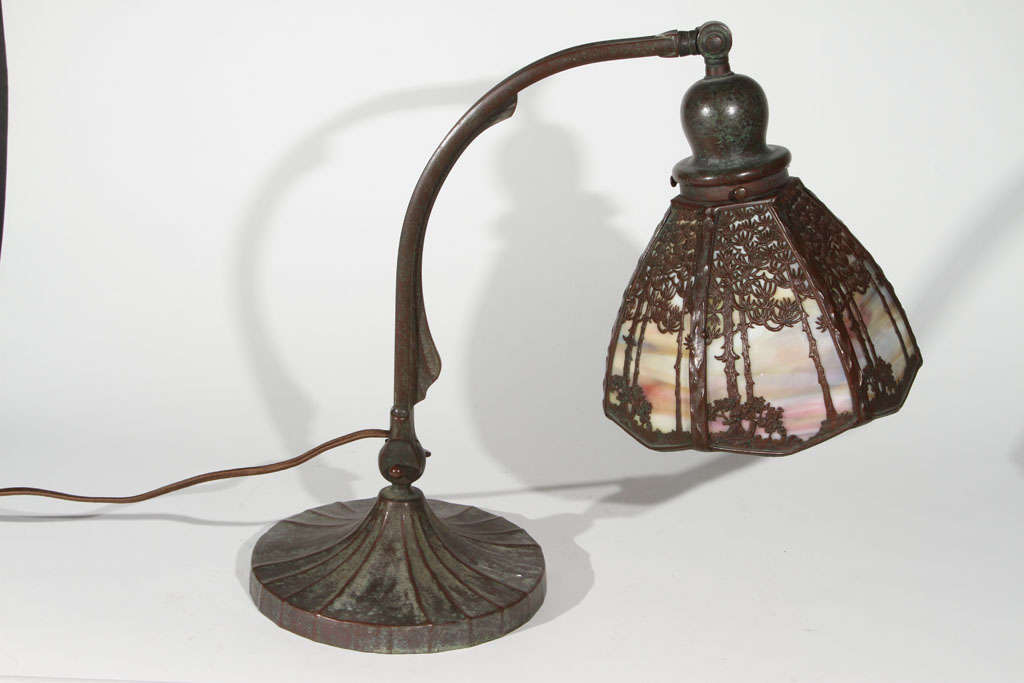 Very good original Handel desk lamp featuring a colorful sunset glass shade with intricate forest overlay design. Double knuckle adjusters, original socket, in good working order, both base and shade are signed. Shade is 7.75