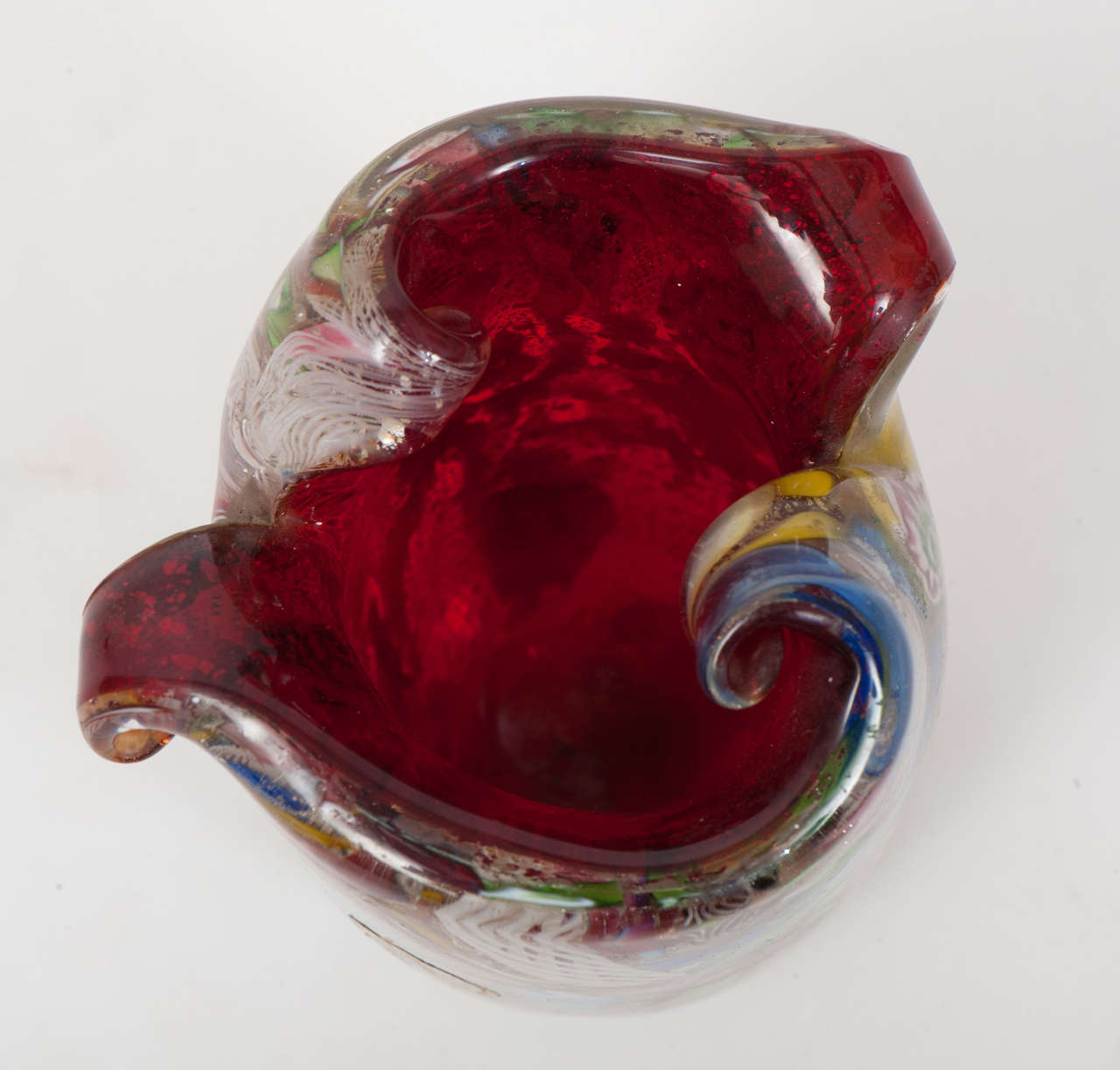 This very unusual small (13cm) vase is sculptural in style, with its scrolled rim, and very heavy for its size. Cased clear glass over red with aventurine in the red layer and latticino and multi-coloured inclusions in the clear layer, it creates a