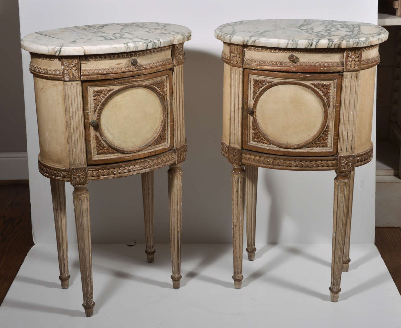Pair of night stands featuring carved details and partial paint with gold accents. Single drawers over the doors for extra interior storage. Beveled marble tops are 7/8