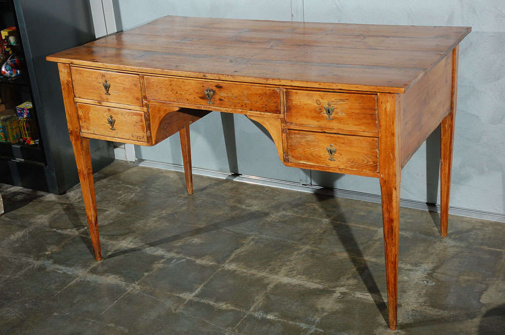 This Spanish knee hole desk, late 18th-early 19th century stands on square tapering chamfered legs. It has five drawers with metal locks, brass urn shape escutcheons and two iron keys. The rectangular top is missing the original elements for files