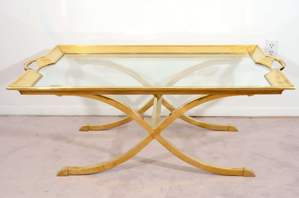 A vintage coffee or cocktail table with a brass framed glass surface that can be lifted off the brass x-form base. The piece is by