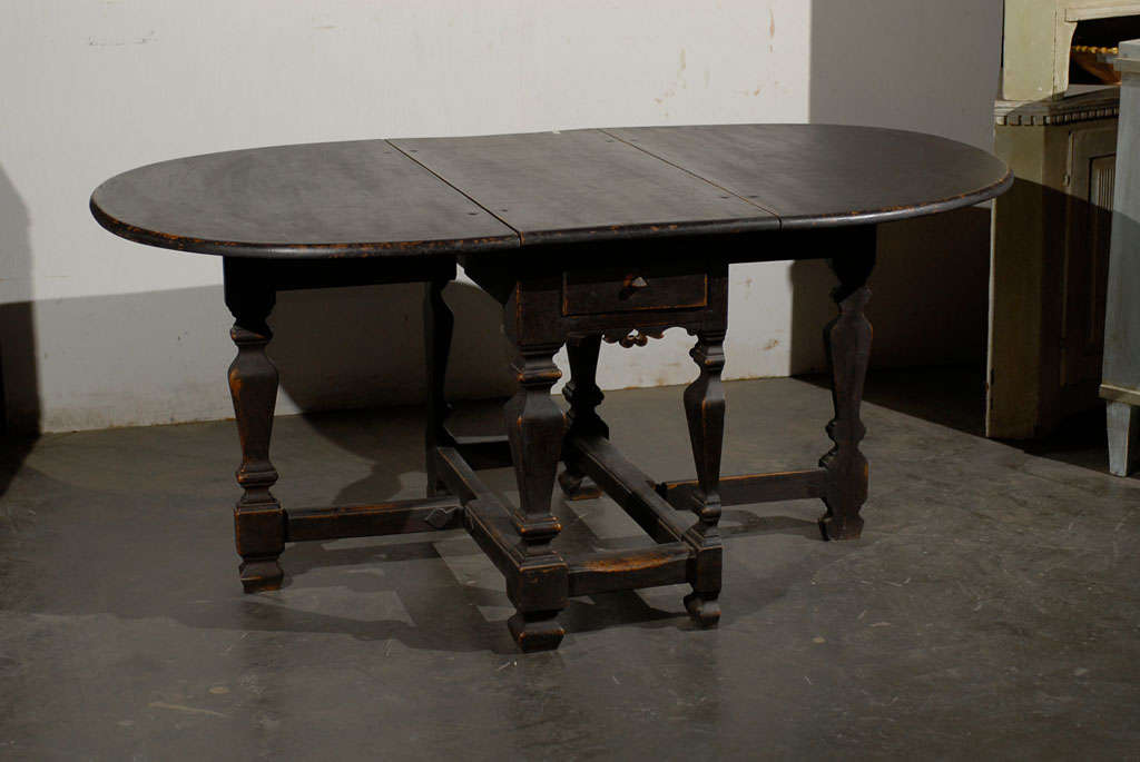 A Swedish 18th century period Baroque painted oak gateleg, drop-leaf table with two drawers with carved apron and split-leg support on each side. The measurements of this Swedish gateleg table are: 66.25