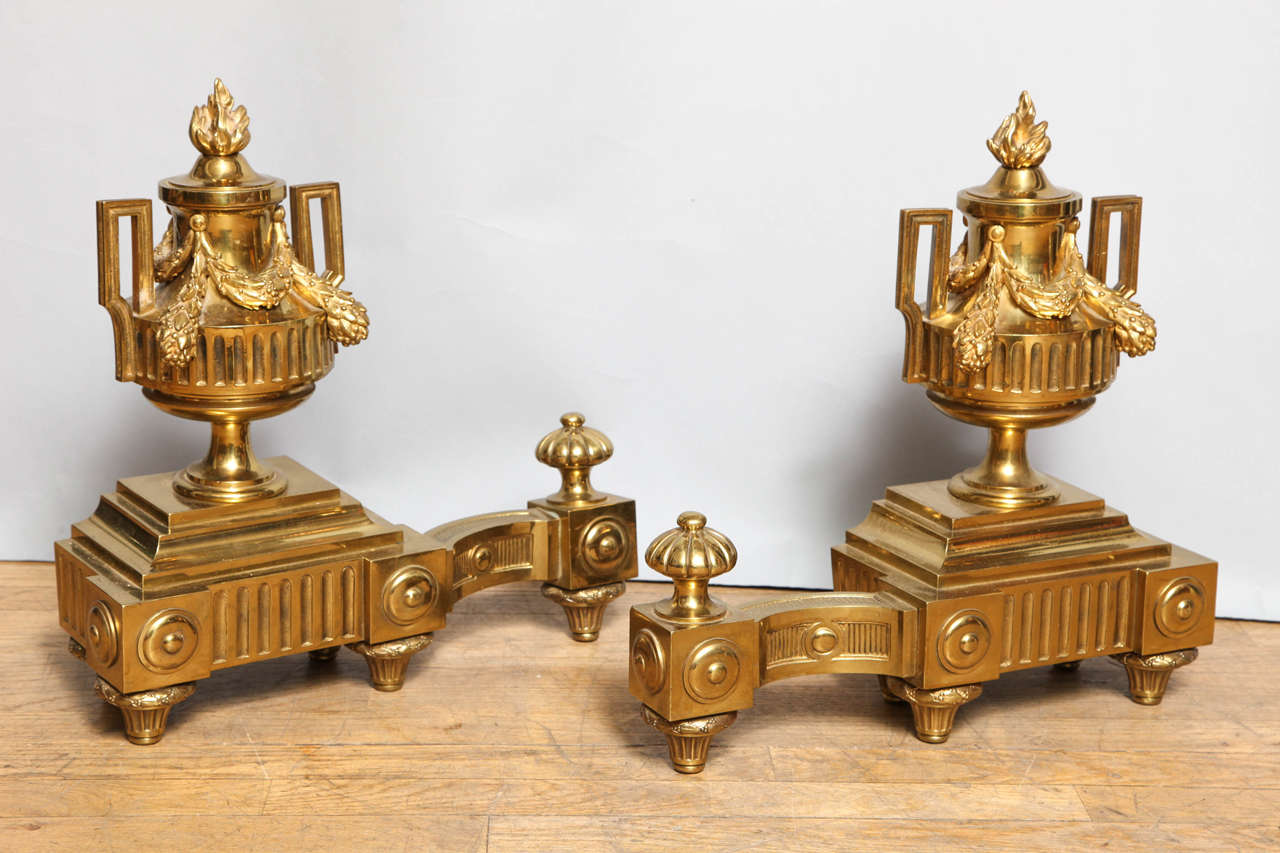 A pair of French Louis XVI style andirons in the form of urns with garlands draped between the handles, supported by square bases with out swept bracket bases.
