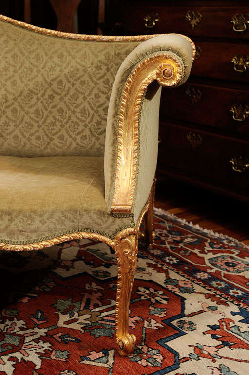 The gadrooned frame with outscrolled armrerests and overupholstered serpentine seat, raised on four cabochon-carved cabriole legs ending in scrolled toes, the cabriole back legs with scrolled toes. Regilded.<br />
<br />
This stylish settee with