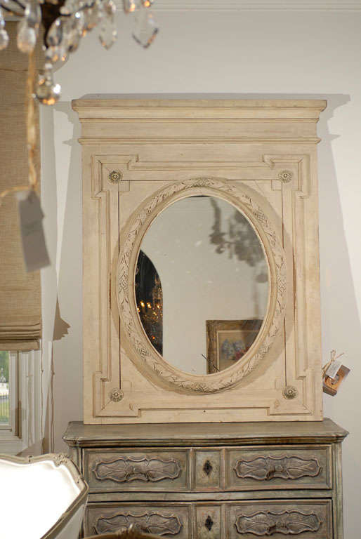 A French Louis XVI style painted wood trumeau mirror from the second half of the 19th century with oval mirror plate. This French trumeau mirror features a linear painted wood frame adorned with a rectangular molding enlivened by accented corners