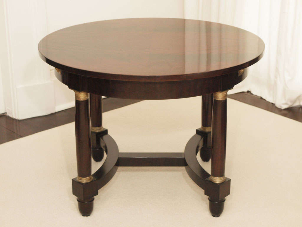 Lovely circular center table in mahogany and mahogany veneers with two leaves extending to rectangular form; bookmatched patterning at the top; columnar supports with gilt detailing; H-shaped stretchers