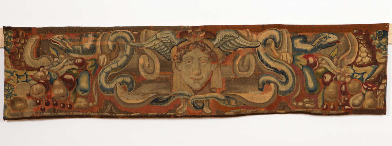 Eine sehr schöne Wandteppichplatte, ursprünglich Teil des oberen Teils einer Bordüre, die in ihrer Mitte den Kopf von Merkur, dem römischen Gott des Handels, darstellt. Der geflügelte Kopf wird von einem Schlangenpaar und einer Reihe von Früchten
