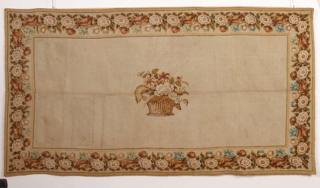 A refined English needlework distinguished by the horizontal arrangement of a centralised motif, this being composed of a delicately rendered floral bouquet in a basket on an ivory open field, framed by rose garland border.