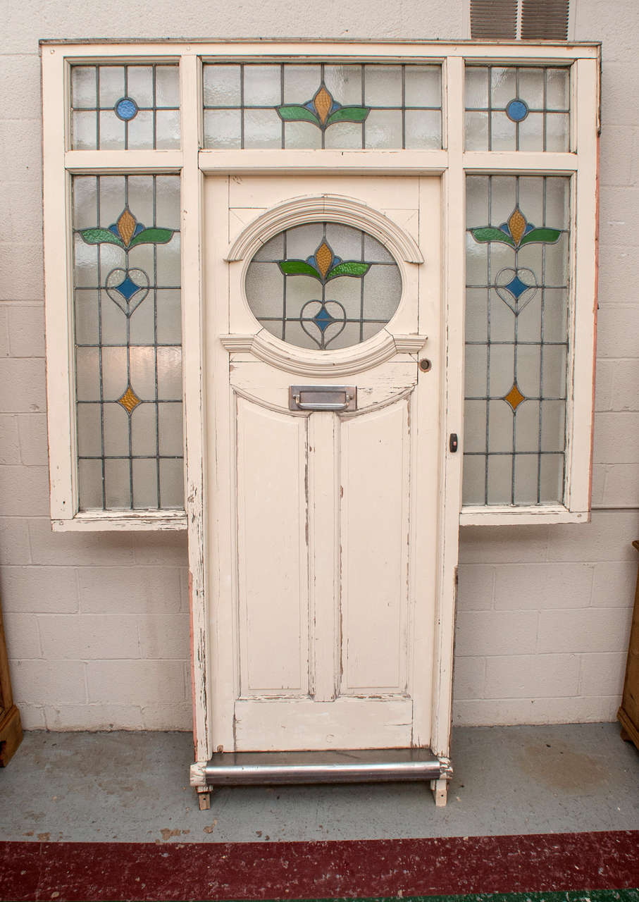 An English front door with oval stained glass panel and stained glass transom and side lights, original knocker/letterbox and hinges.