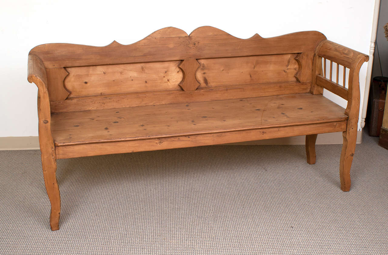 A handsome pine bench featuring a scalloped two panelled back, a generous seat and shapely spindled armrests and decorative legs.  Perfect for an entry hall or waiting room.