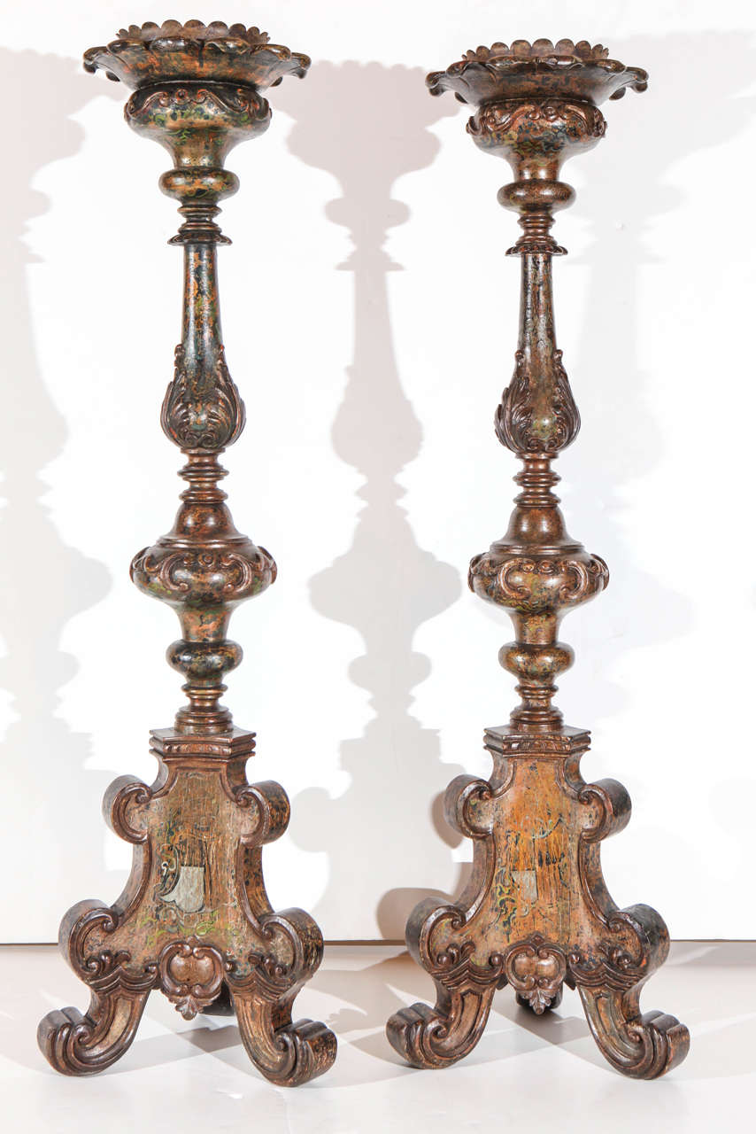 Two, hand-carved and painted, large Tuscan candle sticks featuring foliate details throughout the woodwork. Painted details include heraldic crests and intricate vine and tendril designs.