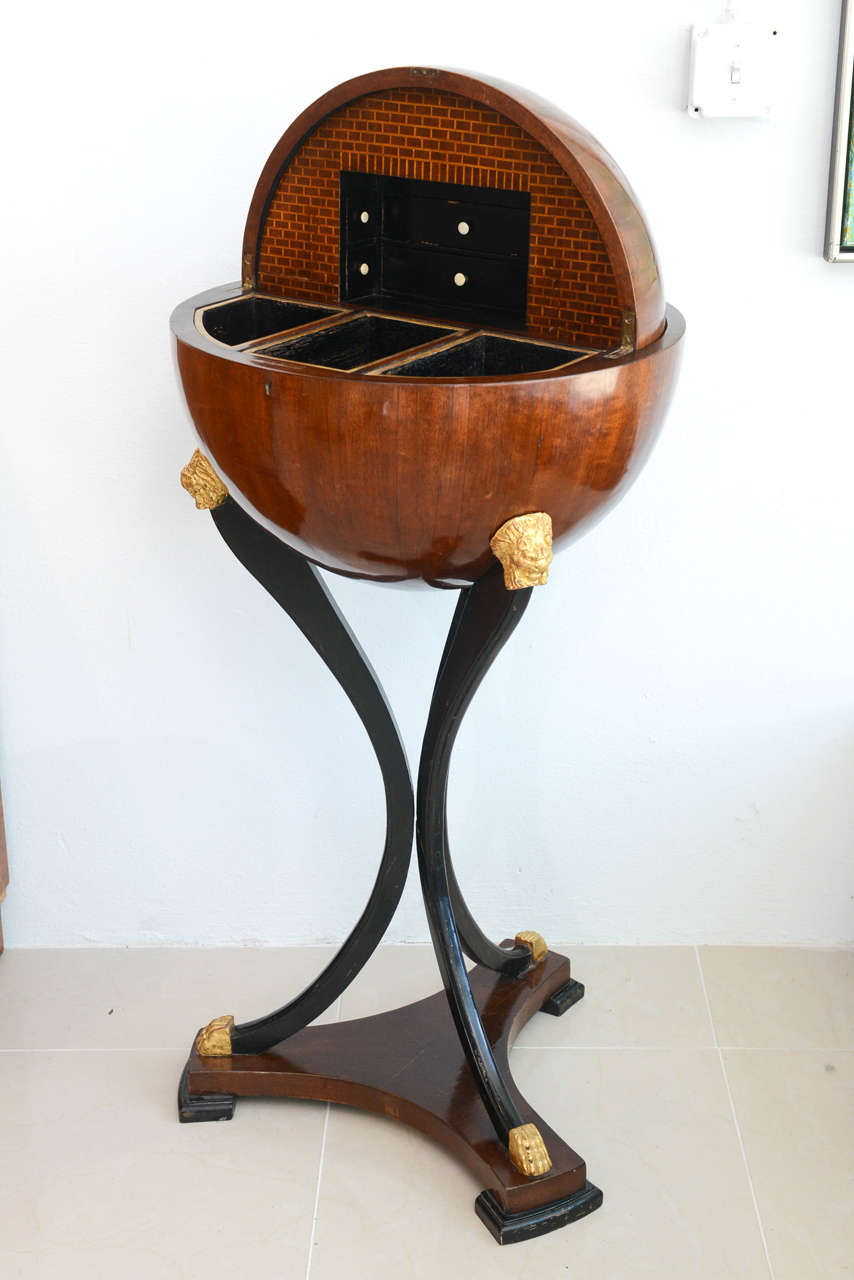 The acorn finial (later), above a globe that opens to reveal a fitted interior, with secret compartments, on tripartite legs with gilt carved lion heads, terminating in paw feet on a tripartite stretcher.