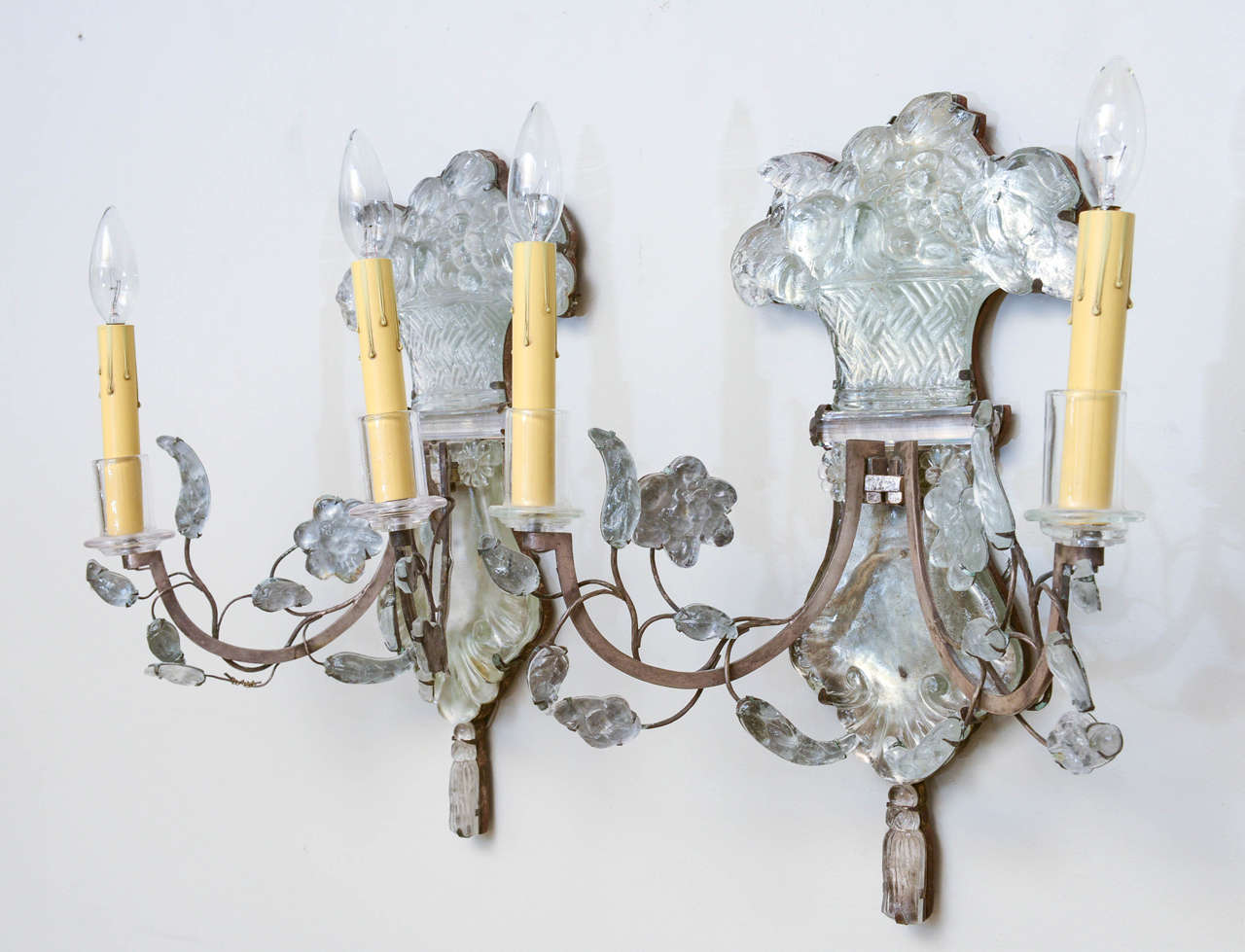 Pair of sconces, likely Bagues; each having two scrolling iron candlearms, draped with crystal leaves and rosettes, its backplate an urn holding a bouquet of flowers, terminating in a tassel.

Stock ID: D9157