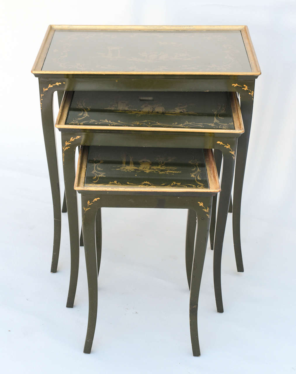 Set of three stack tables of dark green lacquer finish with gilt accents, each top decorated in chinoiserie motifs.