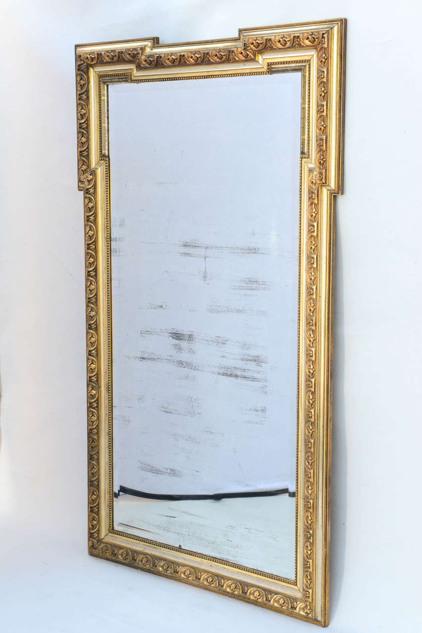 Mirror, in the Neoclassical style, of carved giltwood, its rectangular beveled mirror plate, surrounded by wonderfully carved frame of acanthus filled C-scrolls, bordered with beading and carved rope gadrooning; having an out-stepped and notched