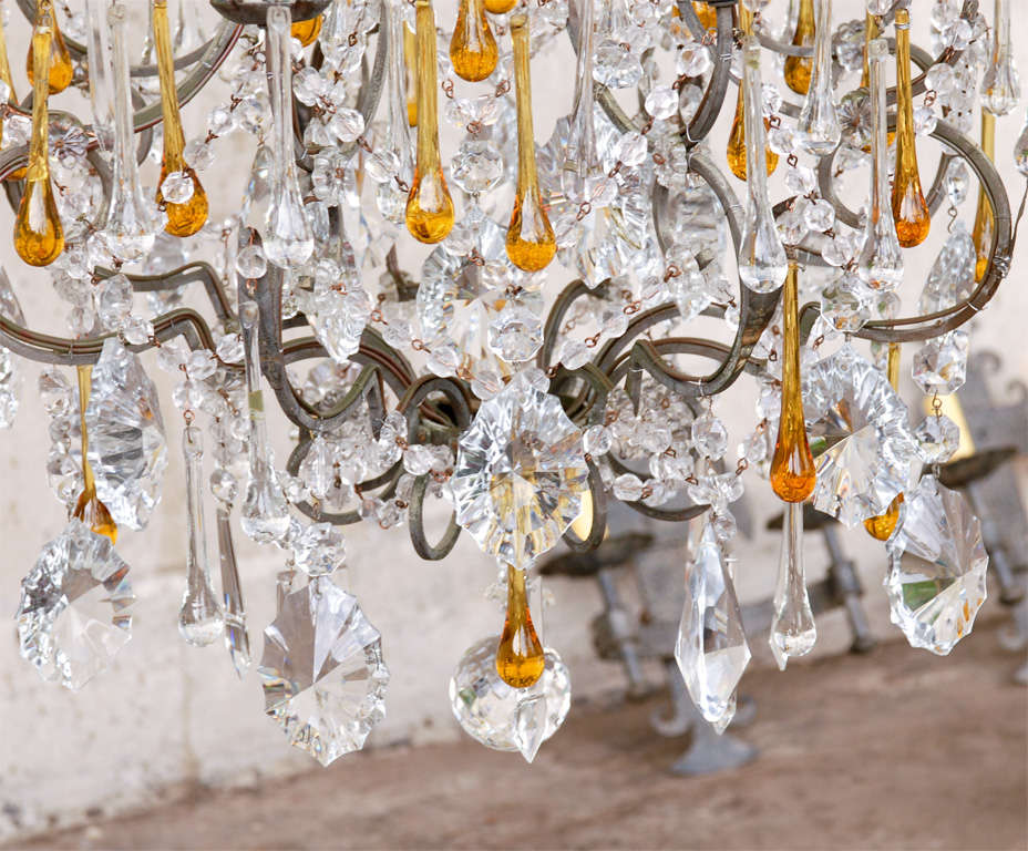 An Italian crystal chandelier. This Italian mid-20th century chandelier features an abundance of various shaped crystals with strands and exquisite amber and clear color tear drop shaped crystals hanging from the iron armature made of thin metal