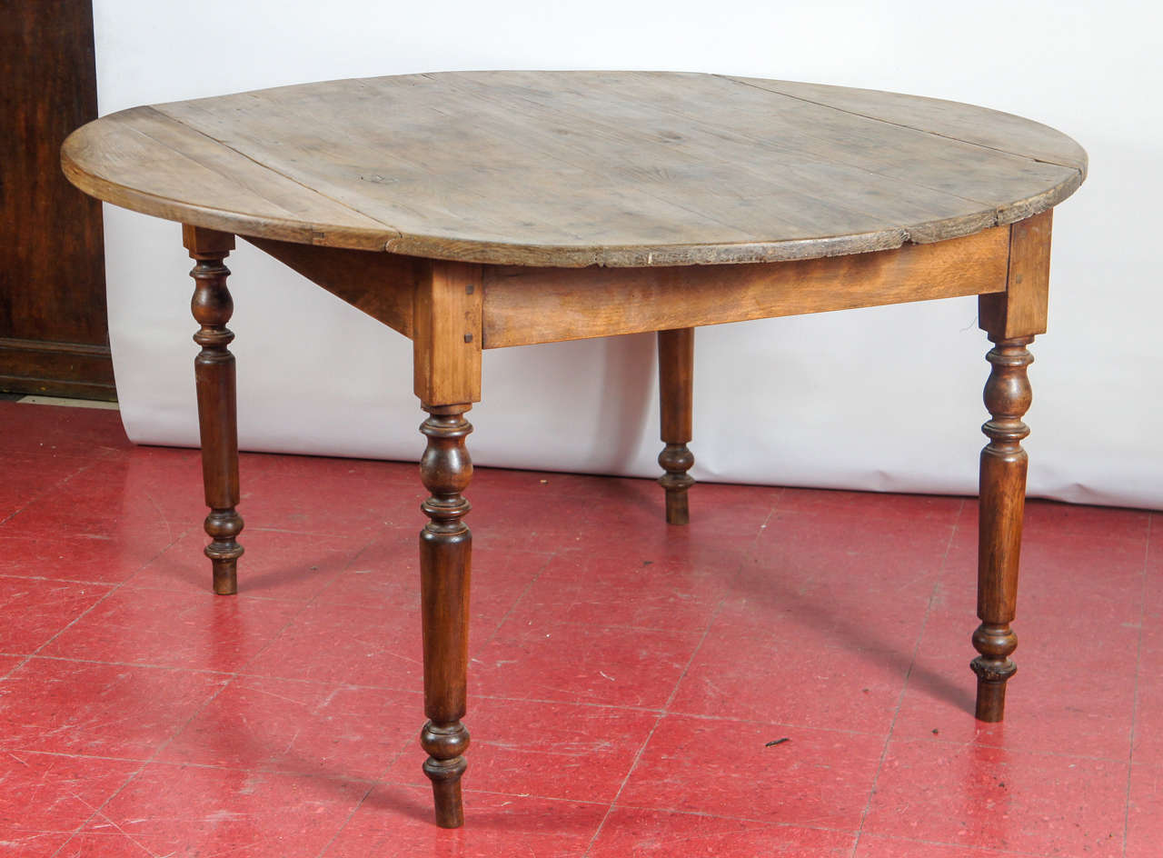 Rustic antique French country round dining table has two iron-hinged round drop leaves supported by pairs of sliding bars that can be pulled out or pushed in by iron handles. The legs are secured to the aprons at the corners by wood pegs.  

With