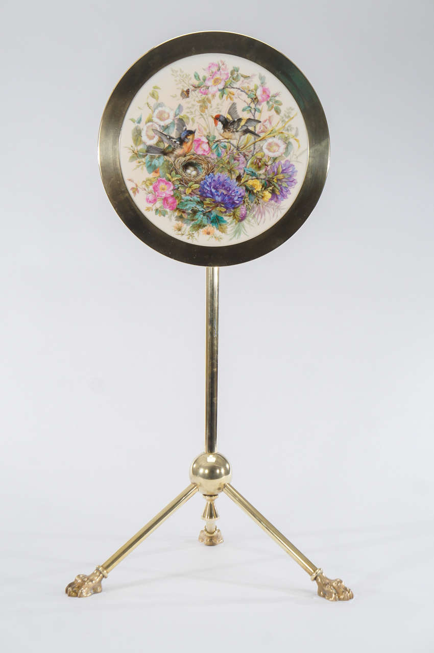 An unusual hand painted porcelain plaque by KPM is mounted into a brass frame, as a tilt top table with 3 splayed claw feet.The beautiful painted subject is two birds surrounded by floral motifs, hovering over the nest filled with eggs. The painting
